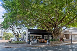 A café with outdoor seating under a large tree, a visible storefront, and parked cars. - Stylish 2BR Apartment + Free Parking on Duke St (Brisbane)