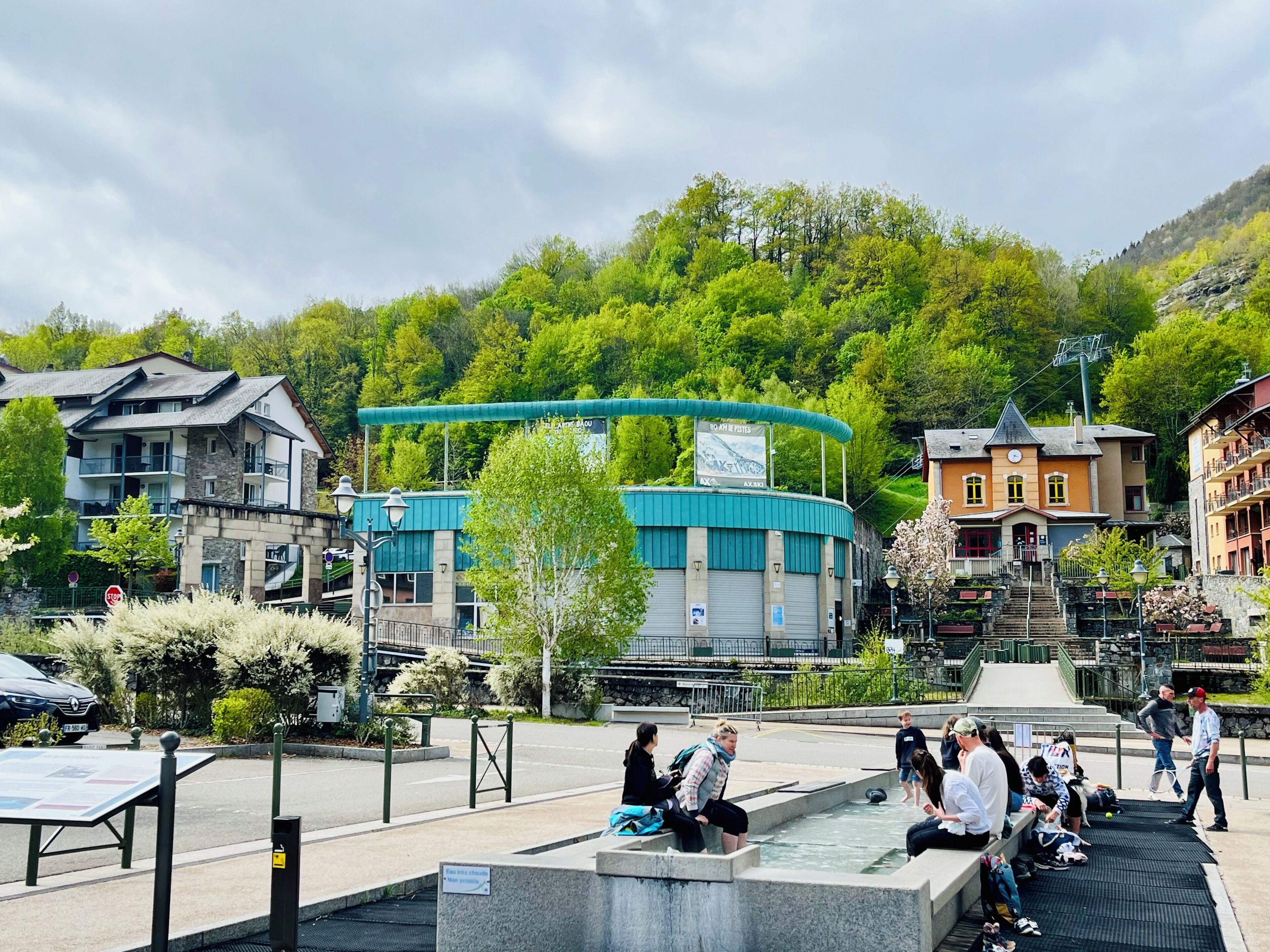 A public square with a fountain, benches, and a building with a blue roof.