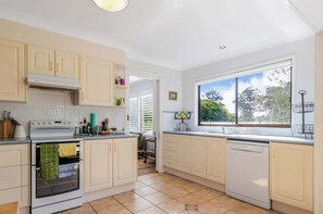 A kitchen with white cabinets, a stove, a dishwasher, and a window with a view of trees.