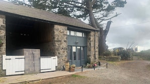 A stone building with a covered entrance, a small porch, and potted plants. - The Stable, Sleeps 2 With Parking (Llanfairpwllgwyngyll)