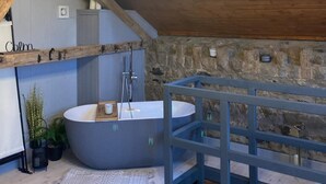 A bathroom with a freestanding bathtub, a wooden shelf, and a stone wall. - The Stable, Sleeps 2 With Parking (Llanfairpwllgwyngyll)