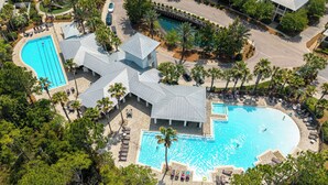 Vista aérea de un complejo turístico con varias piscinas, palmeras y un pabellón cubierto.