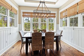 A dining area with a large table, wicker chairs, a chandelier, and large windows with views of greenery. - NatureWalk "Sandy Paws" 3BR + Bunk | Sleeps 10 | Golf Cart | Pets OK | 🐶 (Santa Rosa Beach)