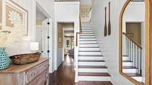 Una escalera con escalones de madera y paredes blancas, un espejo grande y una cesta decorativa sobre un aparador.