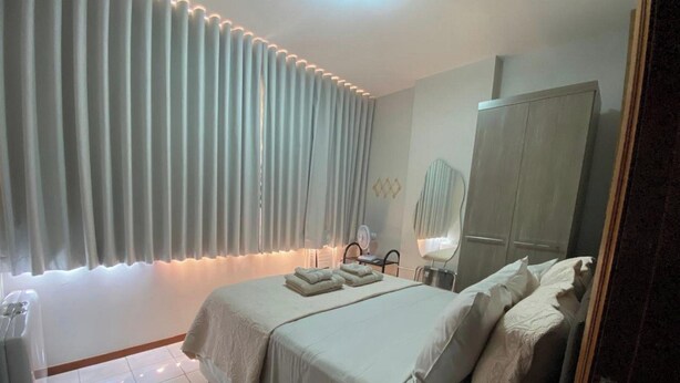 A bedroom with a bed, a wardrobe, a mirror, and a bedside table. - Apartamento Badalar do Sino - Belem - PA (Belém)