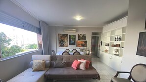 A living room with a sofa, dining table, and kitchen area. - Apartamento Badalar do Sino - Belem - PA (Belém)