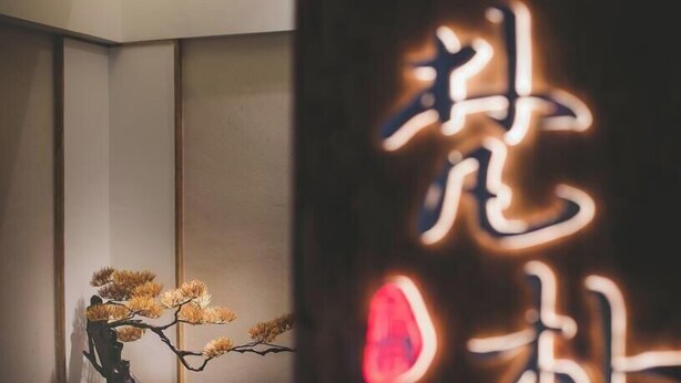 Een kamer met een traditioneel Japans interieur, inclusief een bonsai en kalligrafie aan de muur.