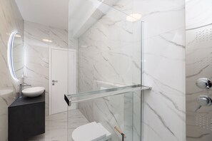 A modern bathroom with a glass shower enclosure, a white toilet, and a marble-tiled wall. - Villa Odeona Zadarvillas (Zadar)