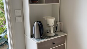 Une petite cuisine équipée d’une machine à café, d’une bouilloire et de placards de rangement.