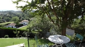 Une terrasse avec une table et des chaises, un pot de fleurs et une vue sur un paysage verdoyant parsemé de maisons.