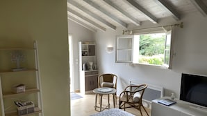 Une chambre avec un lit, une chaise, un bureau avec une télévision, une fenêtre et un coin cuisine.