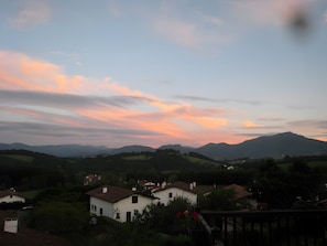 A rural landscape with houses, a mountain in the background, and a sunset sky.