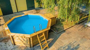 Una piscina hexagonal de madera con escalera, rodeada de baldosas de piedra y una puerta verde.