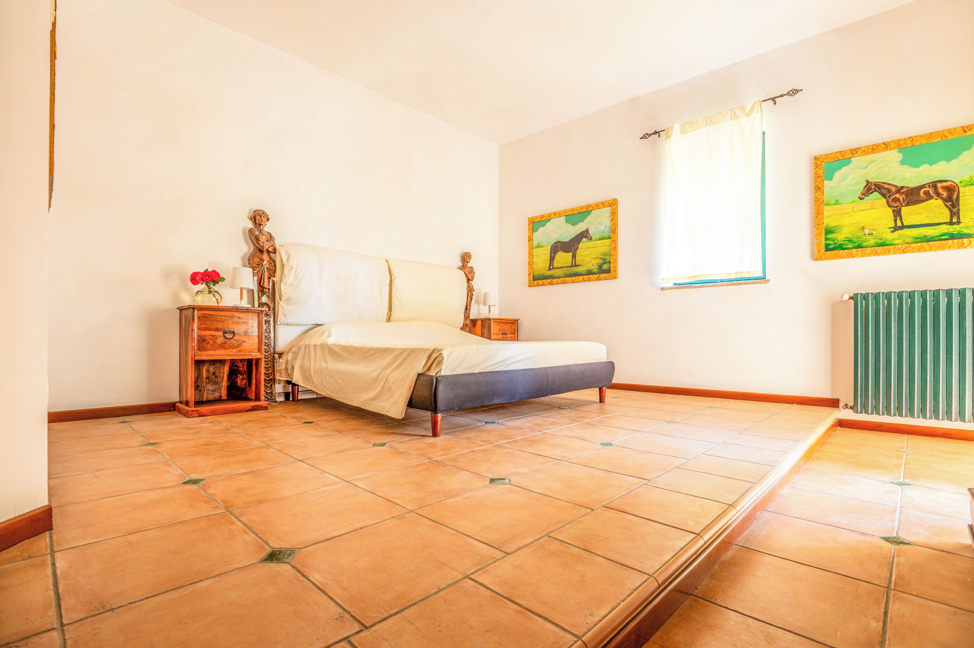 Une chambre à coucher comprenant un lit, une table de chevet, un radiateur et deux tableaux accrochés au mur.