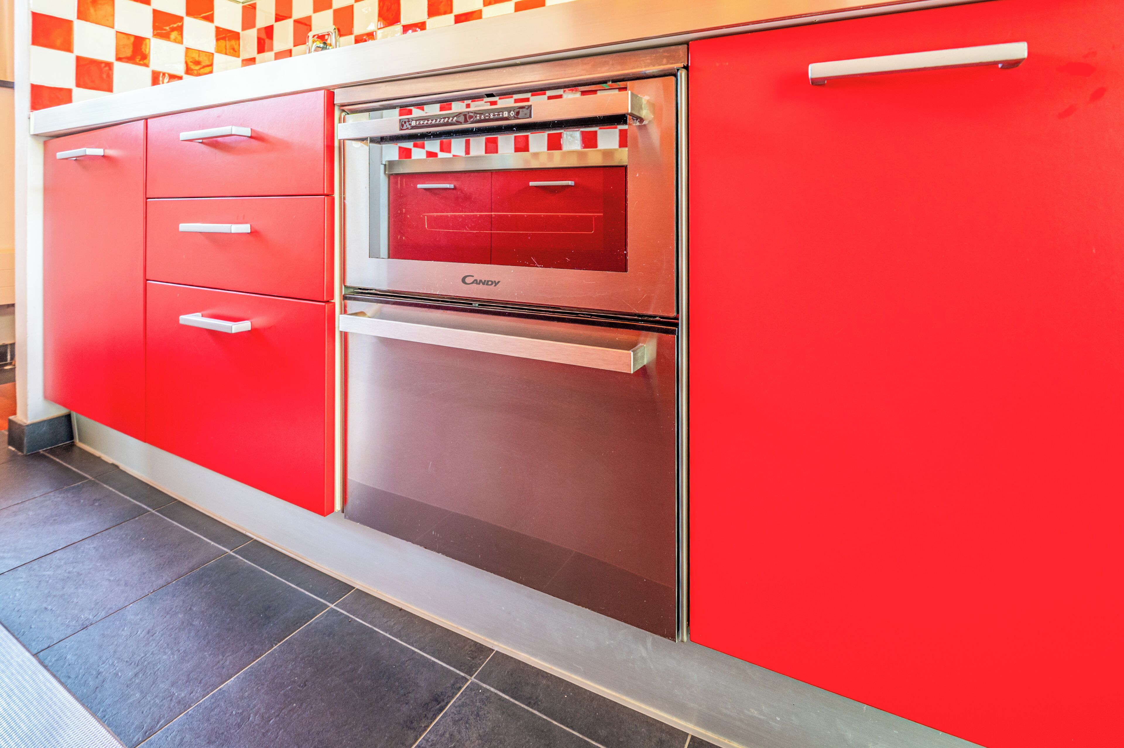 Cozinha com armários vermelhos, forno de aço inoxidável e piso ladrilhado.
