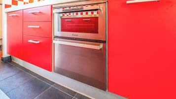 Cozinha com armários vermelhos, forno de aço inoxidável e piso ladrilhado.