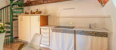 Una cocina con techo de ladrillo, una escalera espiral verde, un armario blanco, un lavabo y una silla de vidrio.