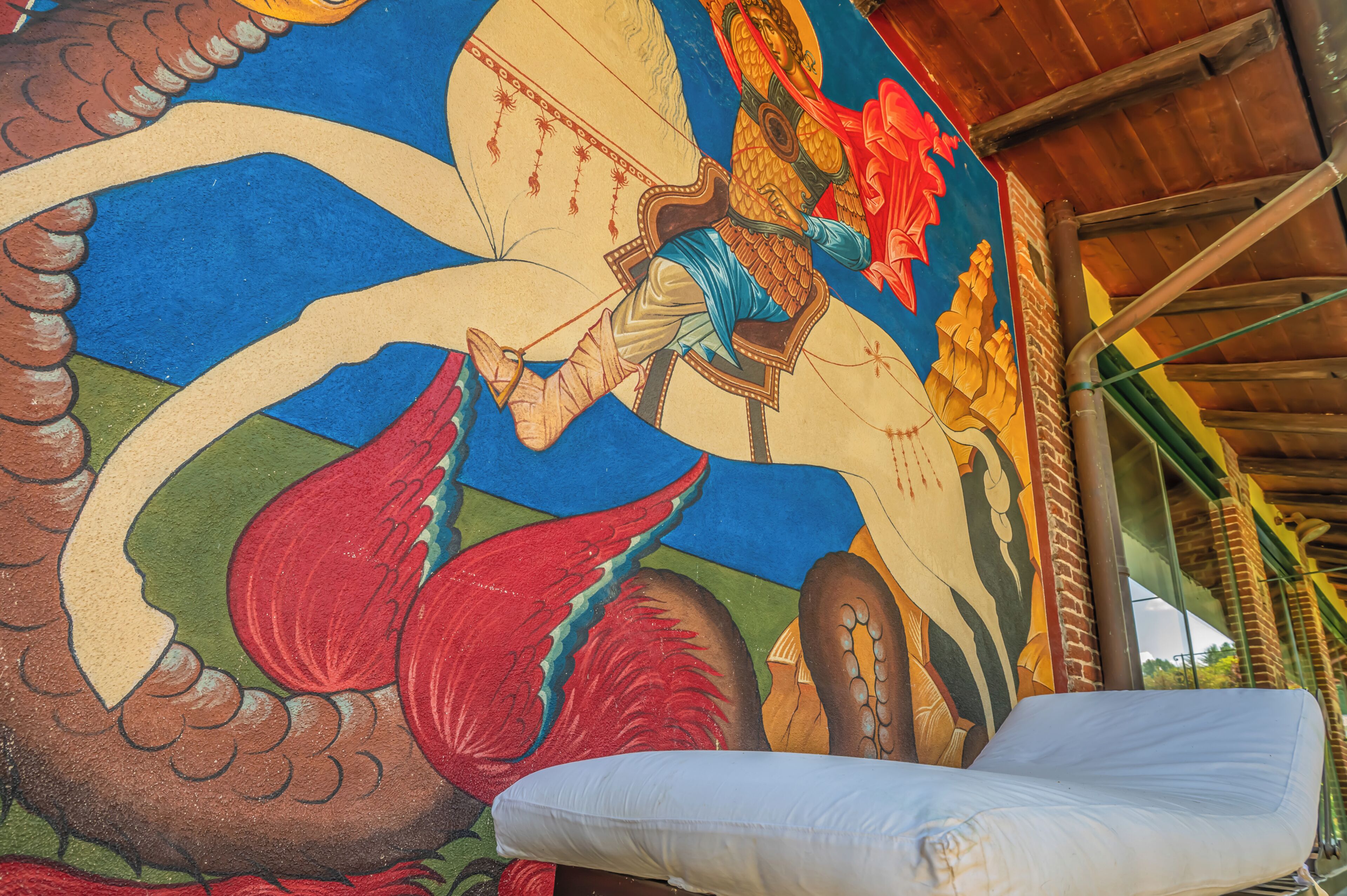 A room with a colorful mural, a bed, and a wooden ceiling structure.