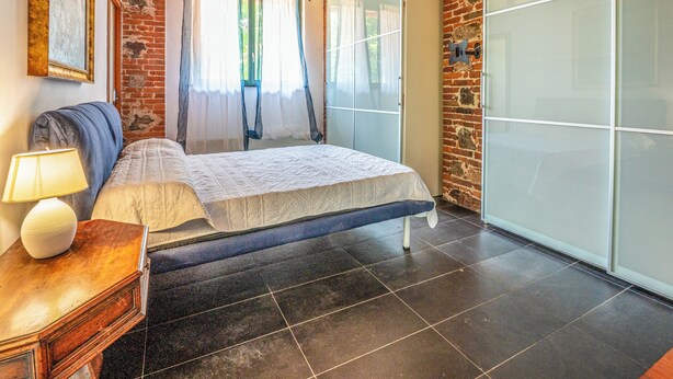 Een slaapkamer met een bed, nachtkastje met lamp, een kledingkast en een bakstenen muur.