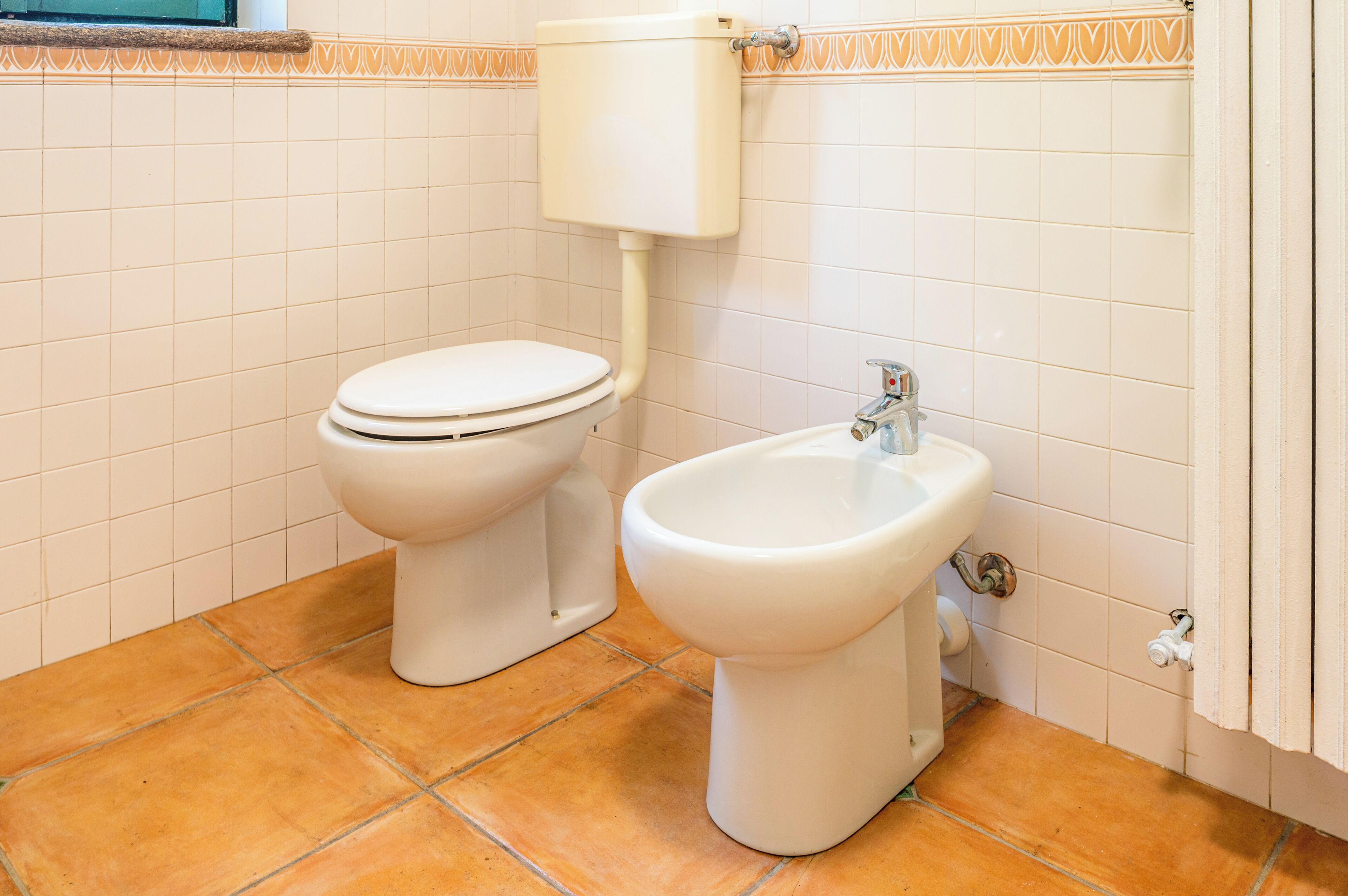 Un baño con inodoro y bidé, azulejos blancos y piso de baldosas.