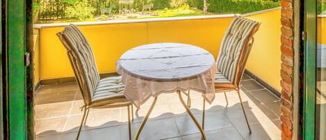Un balcón con una mesa redonda y dos sillas, vistas a la vegetación y una pequeña estructura decorativa.
