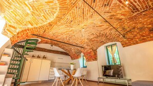 A kitchen with a brick ceiling, white cabinets, a dining table with chairs, and a TV. - Cristal Apartments (Masserano)