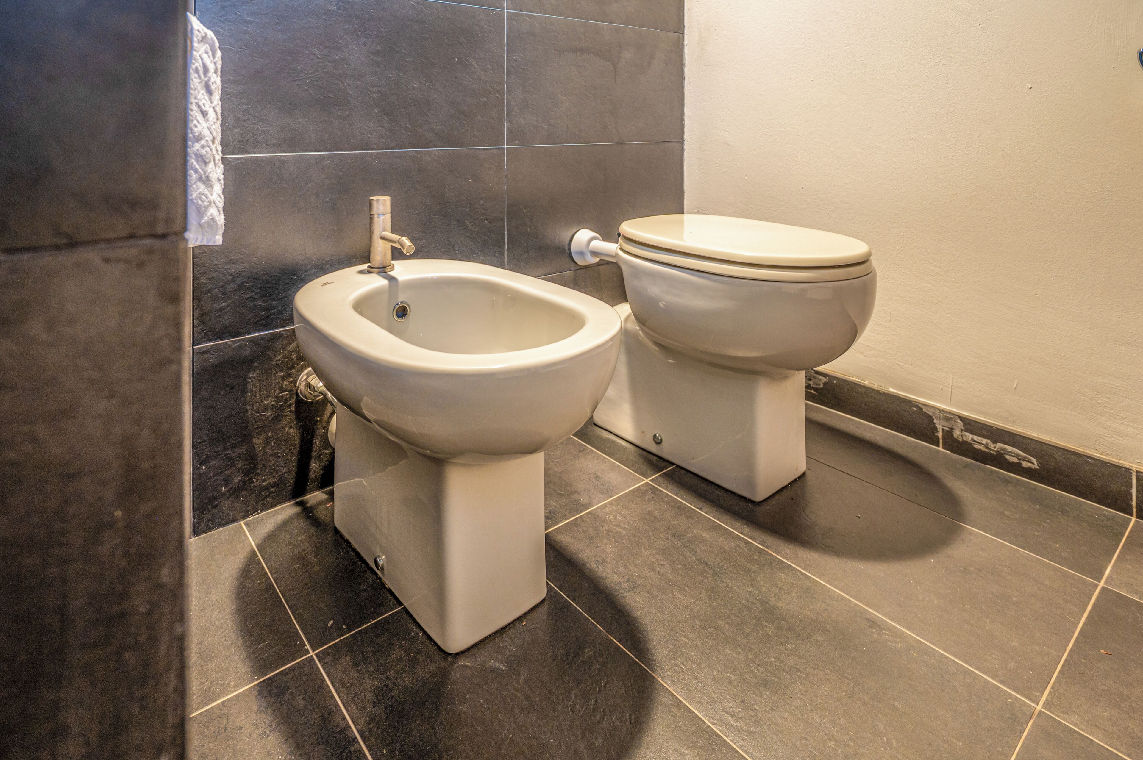 Un baño con bidé, inodoro y suelo de baldosas oscuras.
