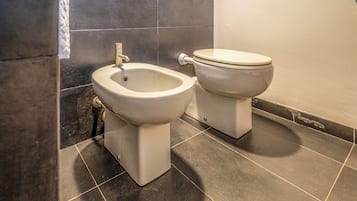 Un baño con bidé, inodoro y suelo de baldosas oscuras.