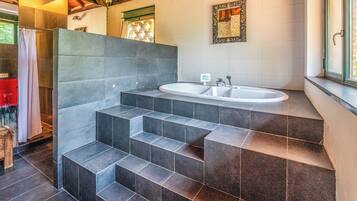 Une salle de bain dotée d’une grande baignoire, d’un escalier à marches recouvertes de carreaux foncés, d’un espace douche et d’une fenêtre offrant une vue agréable.
