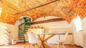 A kitchen with a brick ceiling, white chairs, a glass table, and a green spiral staircase. - Cristal Apartments (Masserano)