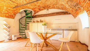 A kitchen with a glass table, white chairs, a spiral staircase, and a tiled floor. - Cristal Apartments (Masserano)