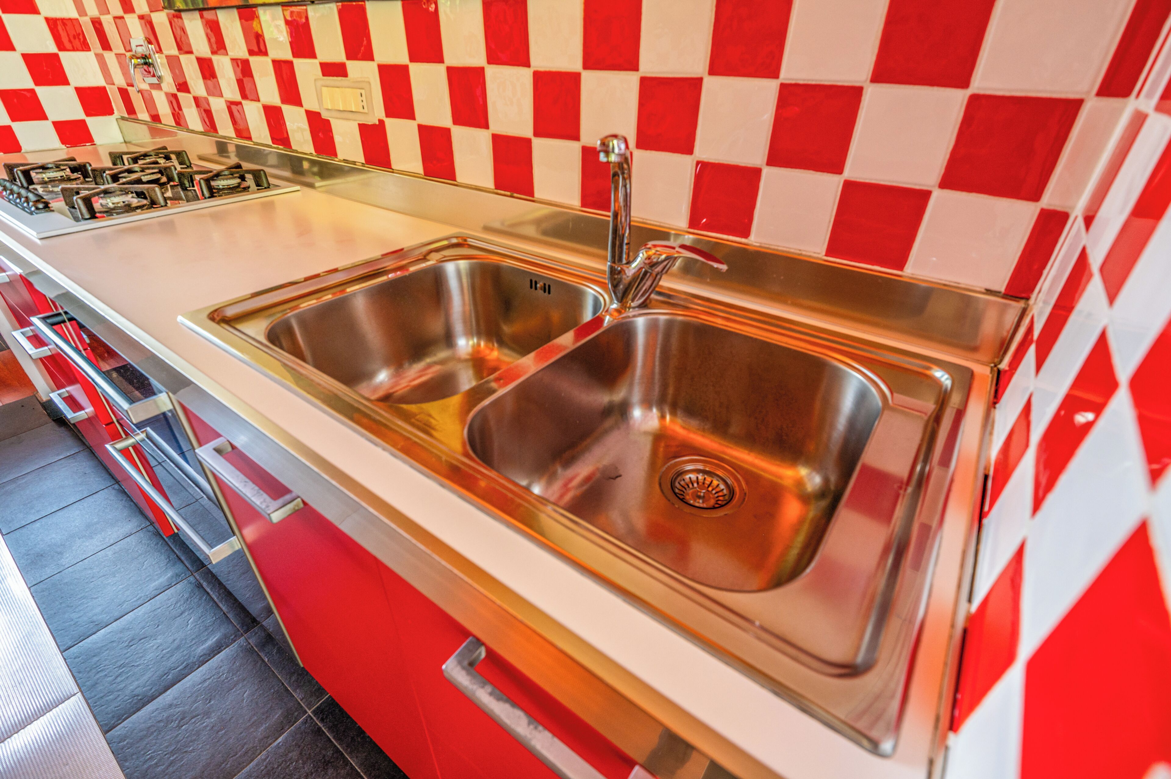 A kitchen with a stainless steel sink, a gas stove, and a red and white checkered backsplash.
