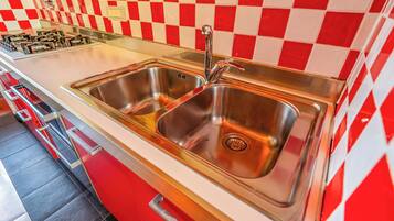 A kitchen with a stainless steel sink, a gas stove, and a red and white checkered backsplash.