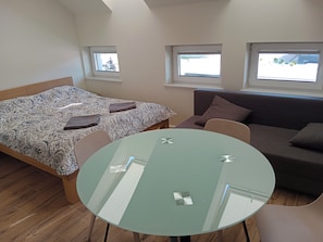 A bedroom with a bed, a sofa, a glass table, and two windows. - Apartamenty Elbląska 20A (Braniewo)