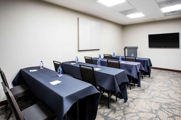Un salón de conferencias con mesas, sillas, botellas de agua y una pantalla para proyector.