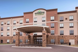 Un hotel de varios pisos con un llamativo letrero de 'Wingate by Wyndham', una entrada cubierta y fachada de ladrillo.