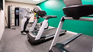 Et fitnessrum med løbebånd, træningsmaskine og en grøn væg.