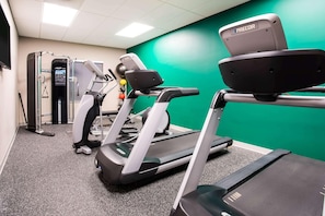 Un gimnasio con cintas de correr, máquinas de pesas y una pared verde.