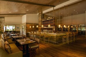 A restaurant with a bar area, wooden floors, and a stone wall. - Carmel Valley Ranch (Carmel)