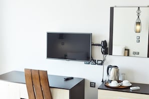 Une chambre d’hôtel équipée d’un téléviseur à écran plat fixé au mur, d’un bureau avec une chaise, d’une bouilloire et d’un plateau avec des tasses et des soucoupes.