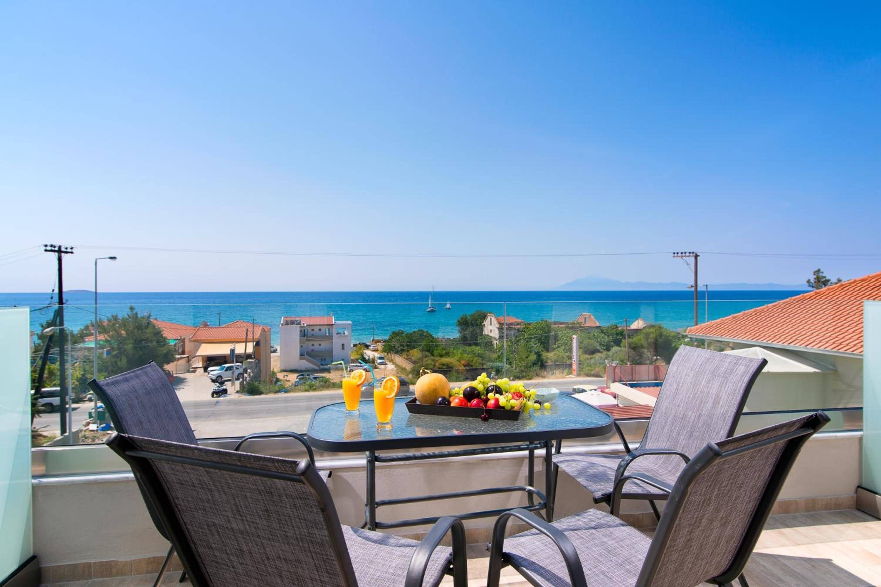 A balcony with a table, chairs, and a view of the sea.