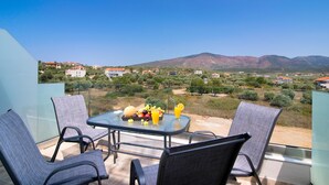 Varanda com mesa posta para dois, com vista para uma paisagem montanhosa e casas ao longe.