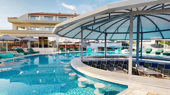 A pool area with a curved design, lounge chairs, and umbrellas. - The Dome Luxury Hotel (Thasos)