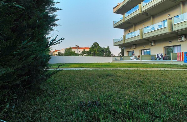 Un edificio residencial con techo plano, varios balcones y una zona verde al frente.