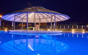 Un área de piscina con zona de estar cubierta, sillas de descanso y un bar.