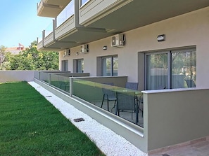 Un edificio moderno con balcón, una pequeña zona de estar al aire libre y un césped cuidado.