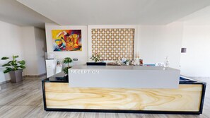 A reception area with a modern design, featuring a reception desk labeled 'RECEPTION' and a large abstract painting on the wall. - The Dome Luxury Hotel (Thasos)