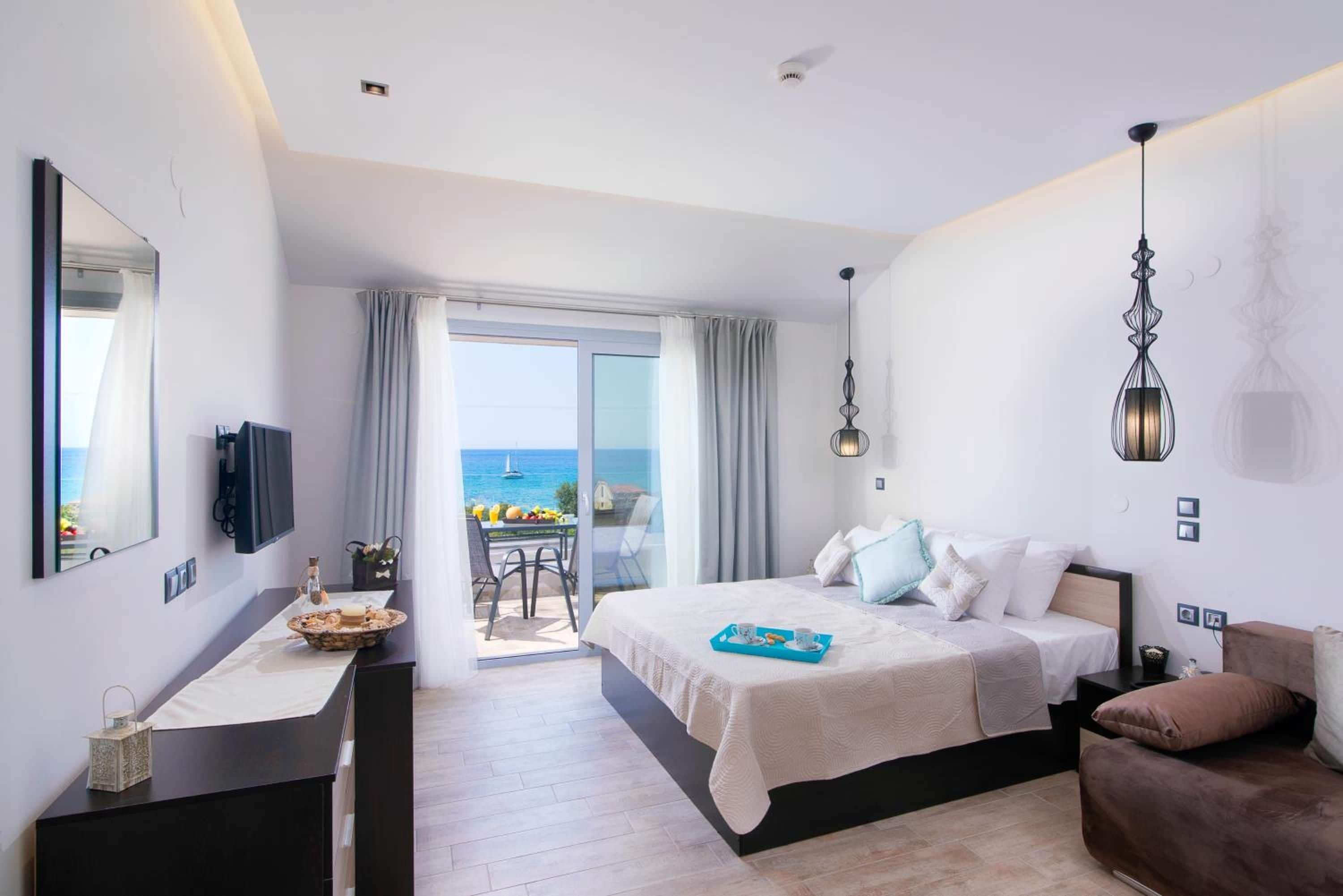 A modern hotel room with a bed, a desk, a chair, and a view of the sea.