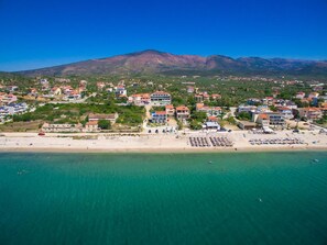 Un pueblo costero con una playa, edificios y una montaña al fondo.