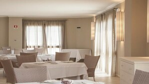 A hotel dining area with tables set for guests, a fire safety sign on the wall, and a lamp on the right side. - Hotel Centrale Sabaudia (Sabaudia)